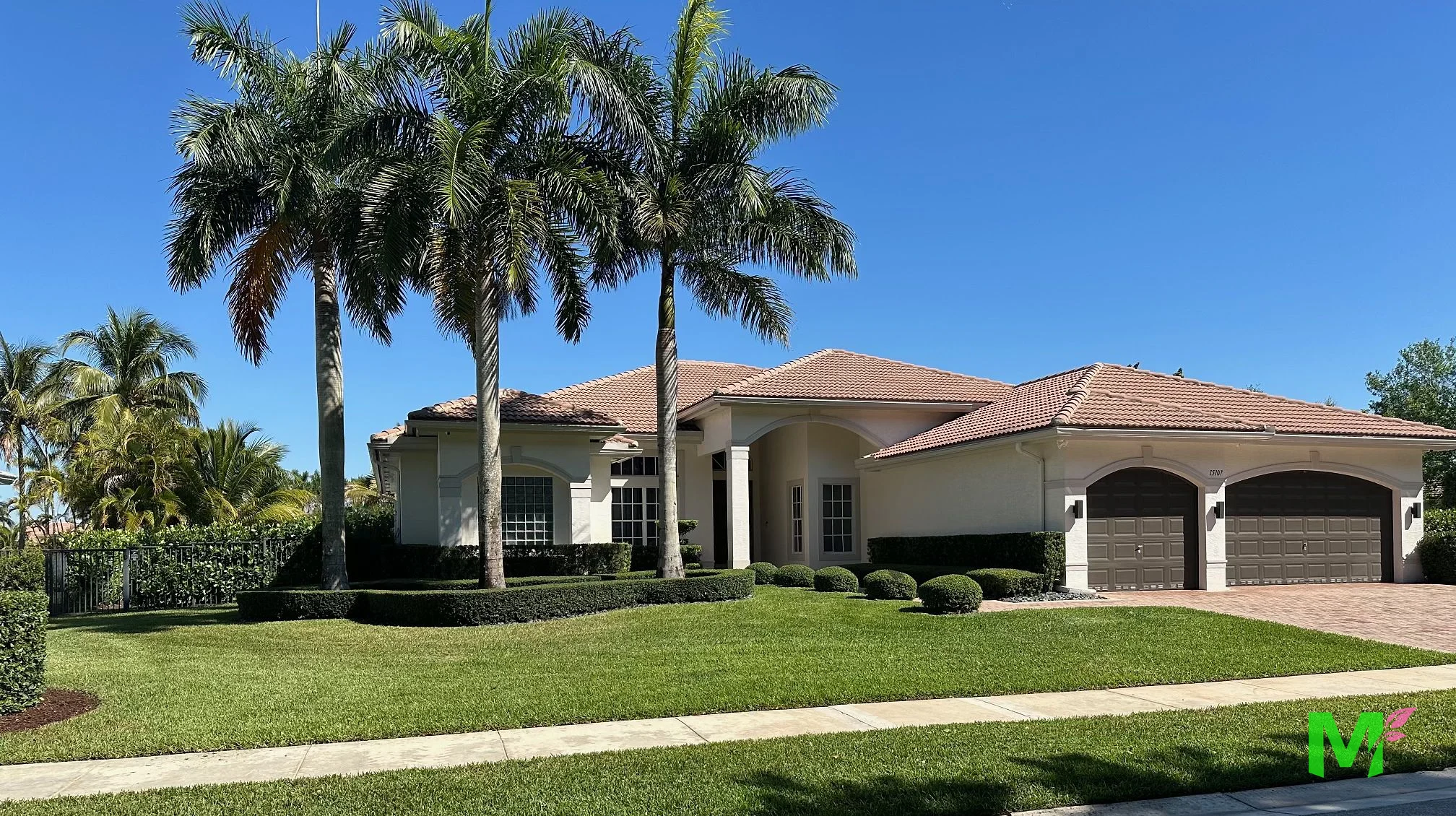 Estate home framed by tall palms, with clipped hedges, rounded shrubs and a manicured front lawn