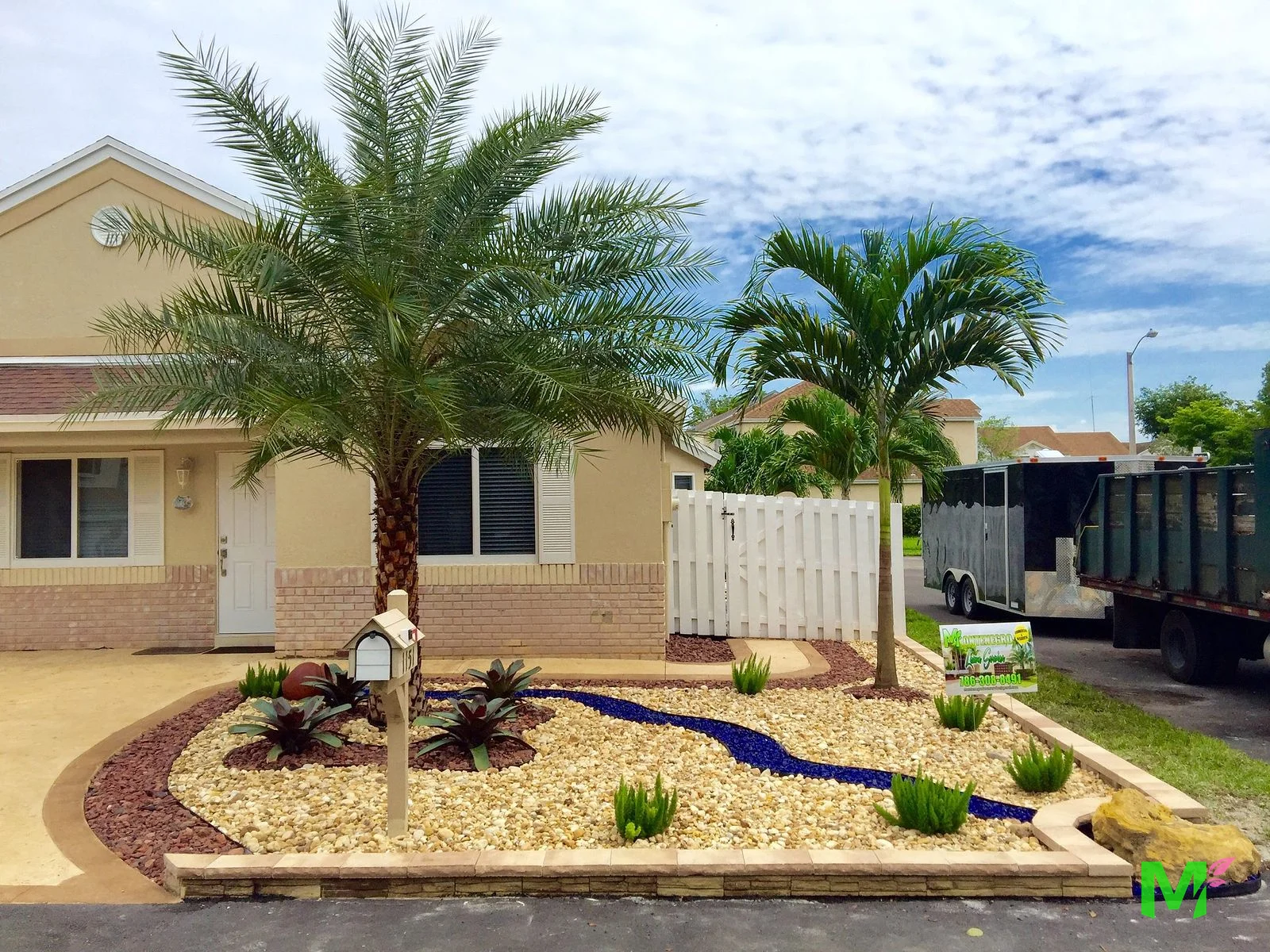Front yard xeriscape with river rock, a cobalt glass dry creek bed, bromeliads, date palm and a paver border
